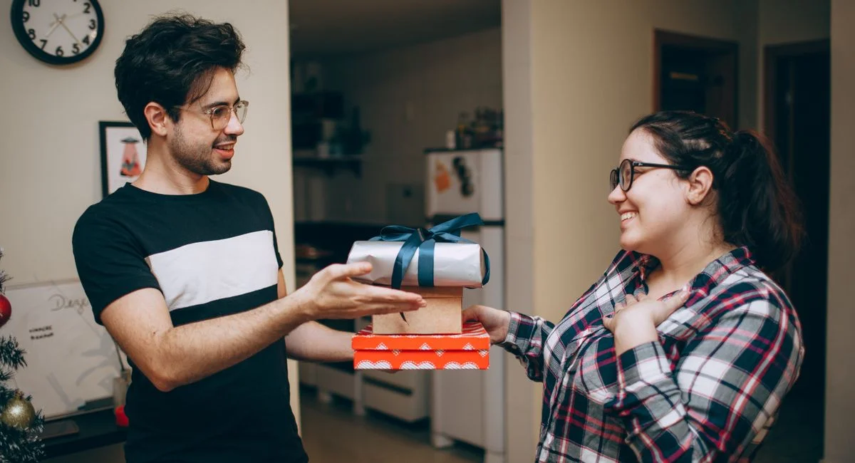 A couple happily exchanging Christmas gifts in a cozy indoor setting, capturing the joy of the holiday season.