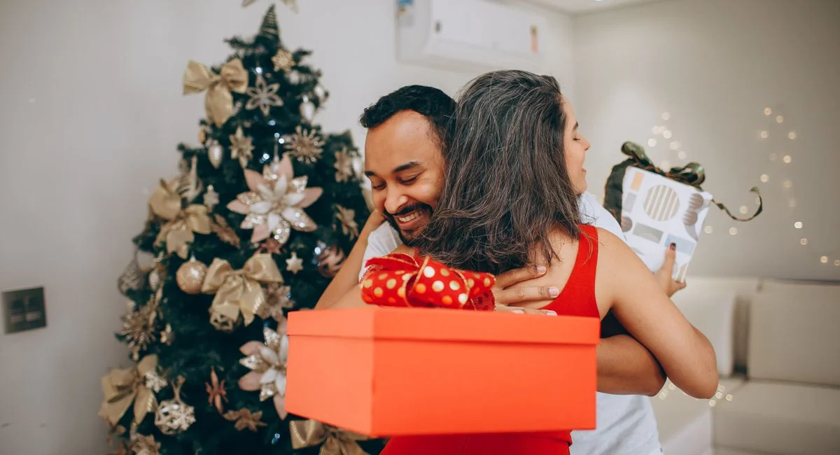 A joyful couple exchanging Christmas gifts beside a beautifully decorated tree, spreading holiday cheer.